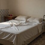 Quarto brasileiro com cama desfeita, relógio e bengala representando risco de mobilidade por sono excessivo