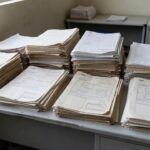 Pilhas de documentos em mesa de agência do INSS representando redução de fila de pedidos